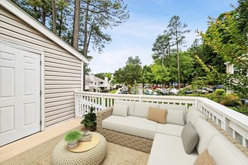 A white couch with pillows is on a patio with a wicker table in front of a house.